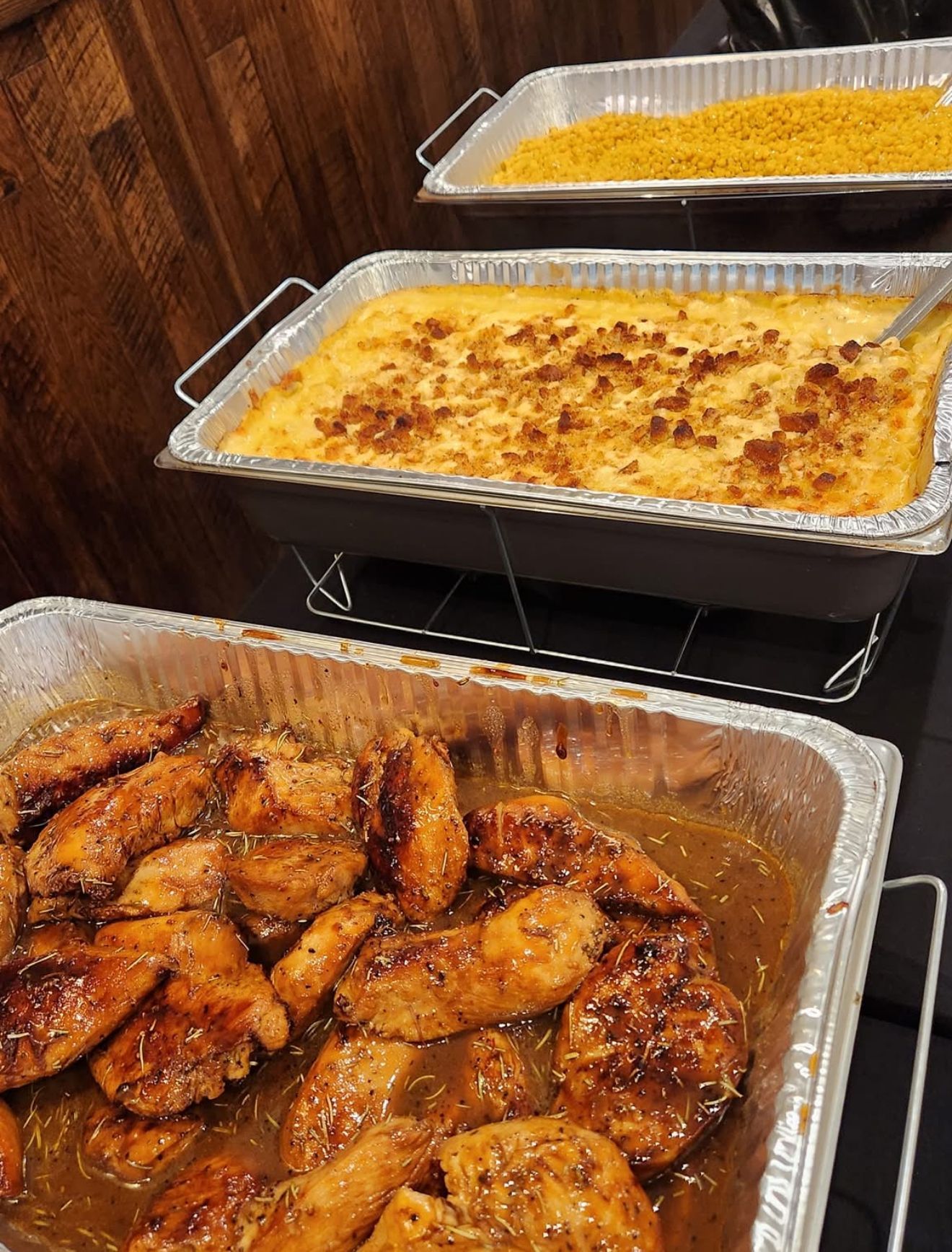 Trays of baked casserole and glazed chicken wings on a buffet serving table