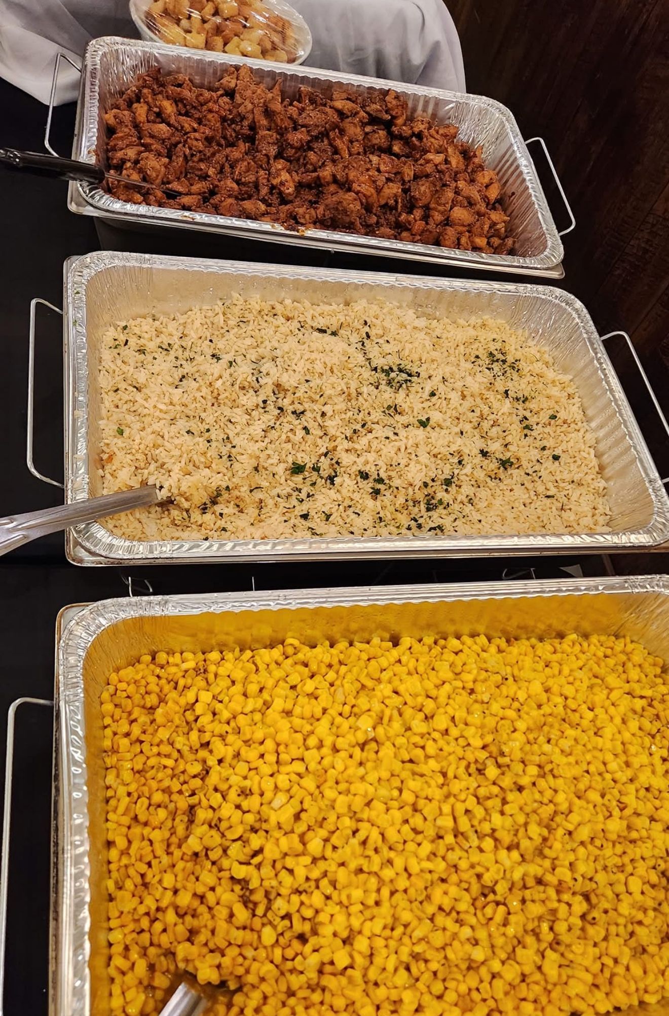 Three trays of food: red-brown, white with herbs, and yellow corn kernels at a buffet