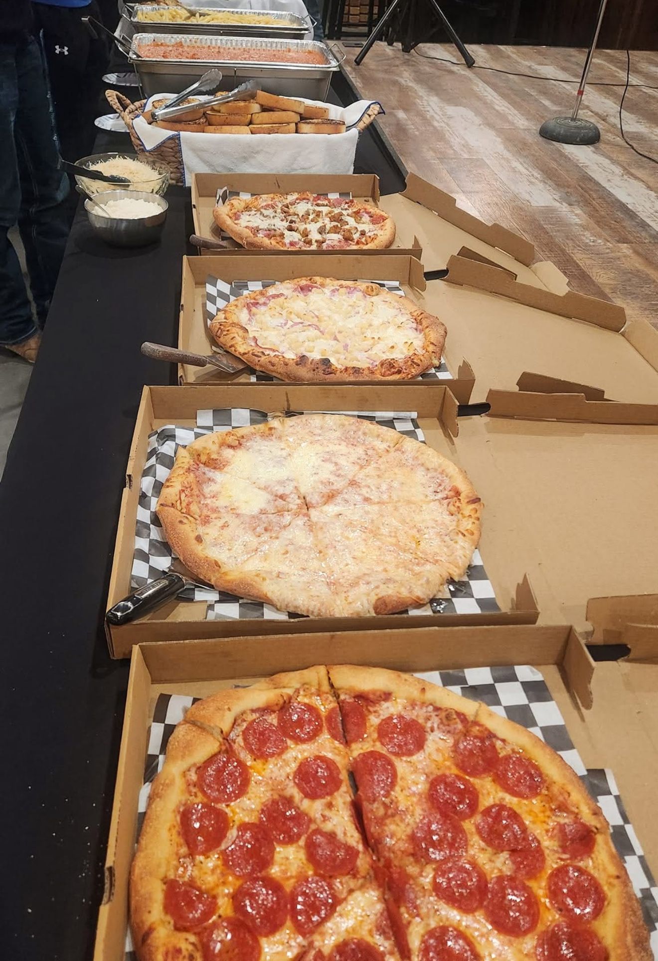 Line of open pizza boxes on a buffet table, with several pizzas and one pepperoni pizza in front.