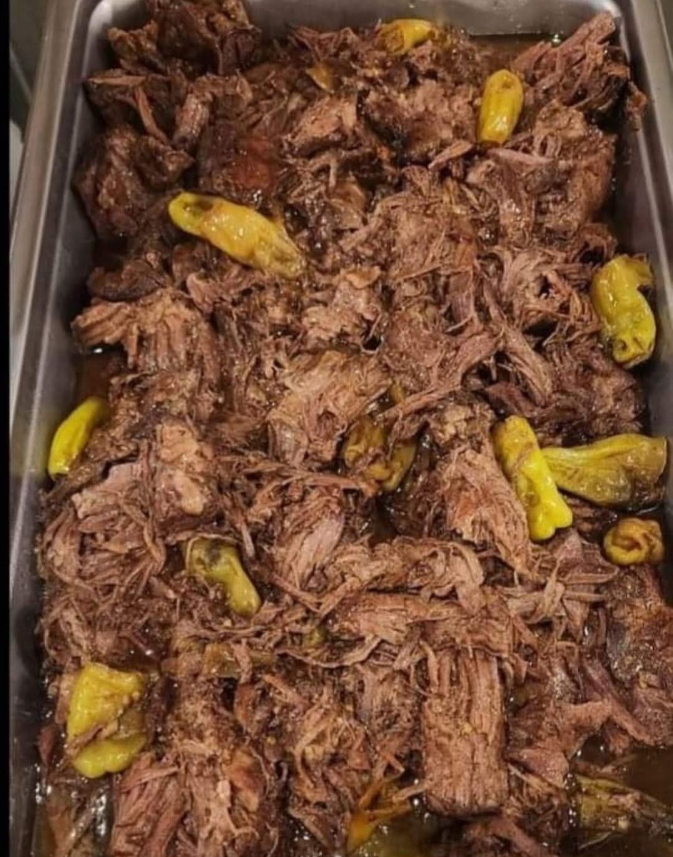 Tray of shredded meat topped with yellow pepper slices in a metal pan