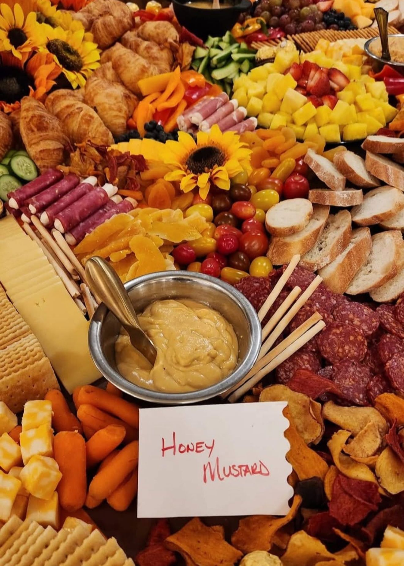 Honey mustard dip on a charcuterie board with bread, fruit, cheese, and sunflower decorations
