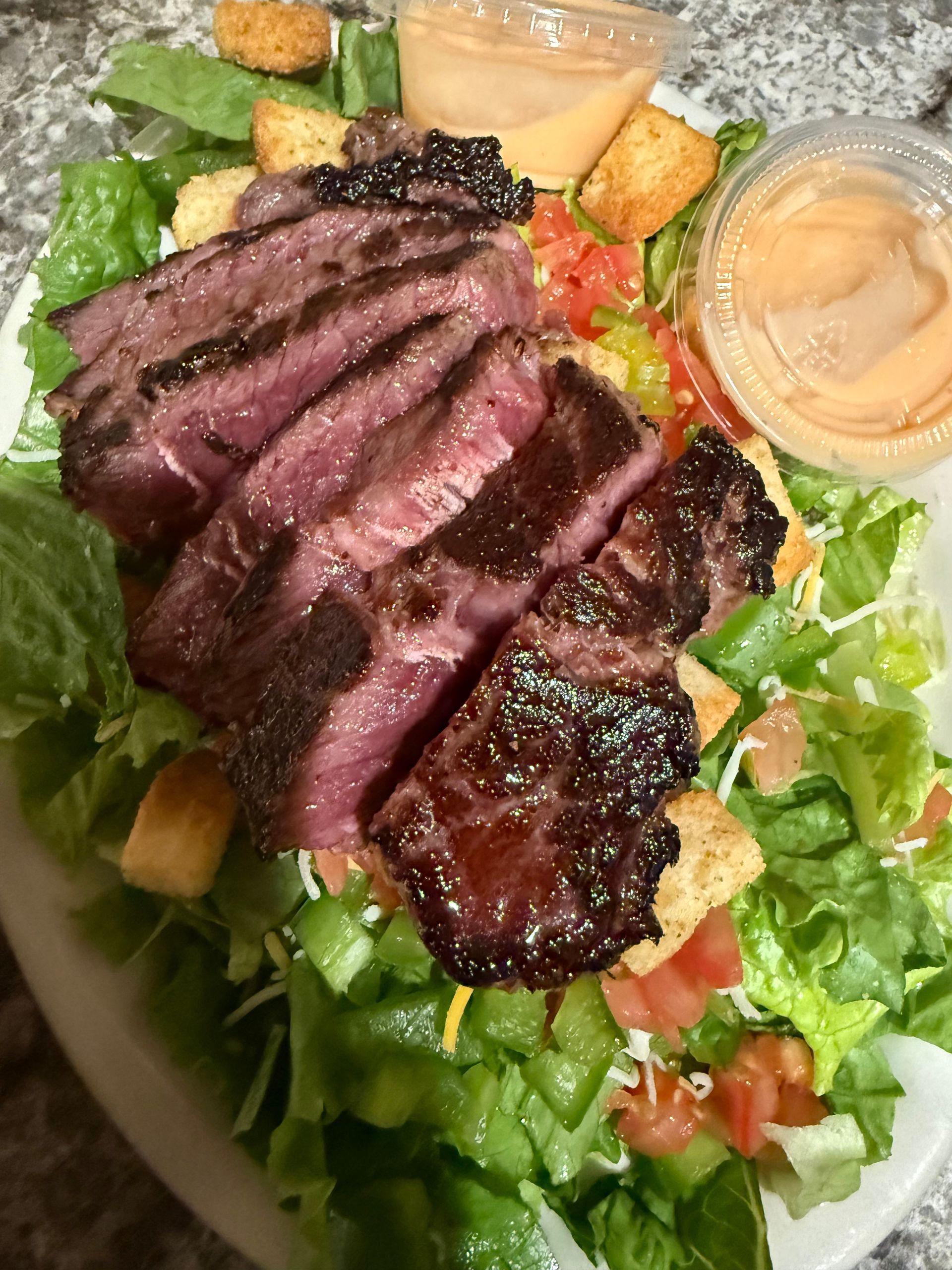 Sliced steak on a green salad with croutons and dressing in a bowl