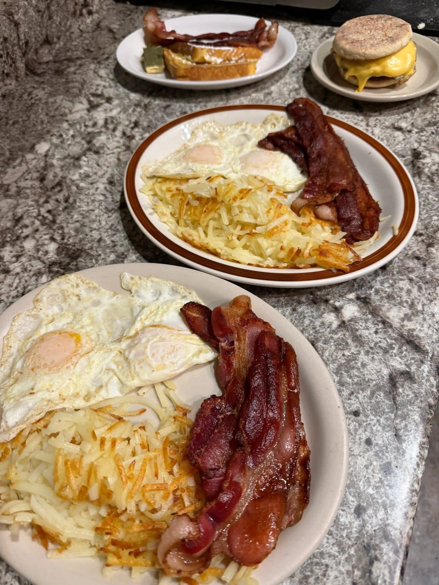 Breakfast plates with eggs, hash browns, bacon, and sausage on a granite countertop.
