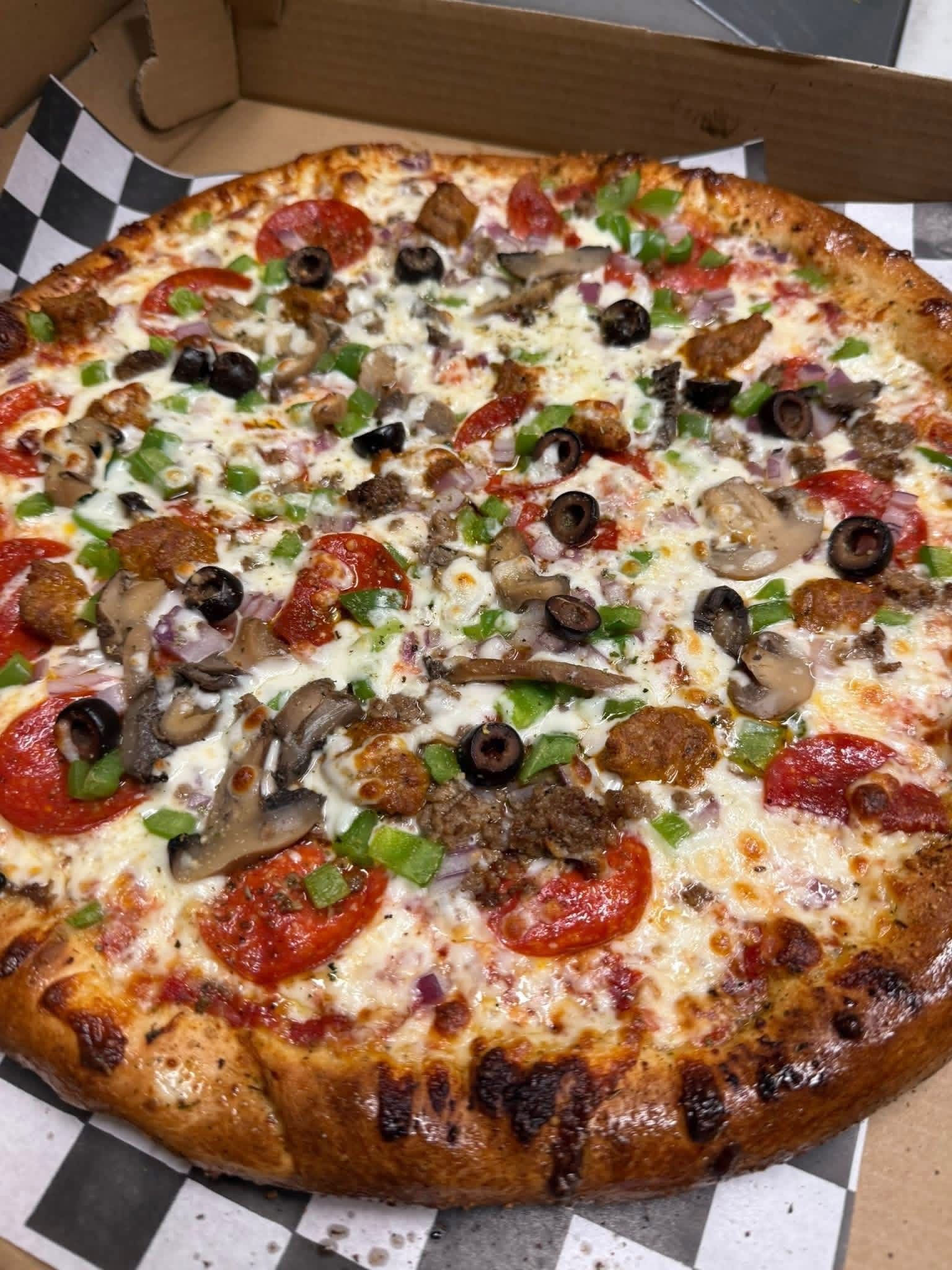 Large pizza with pepperoni, olives, green peppers, mushrooms, and melted cheese on a table