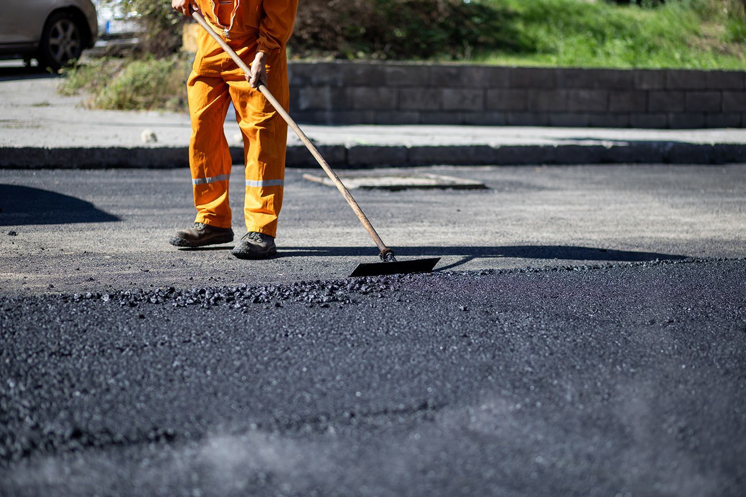 Person in orange jumpsuit smoothing asphalt with a broom on a street. Person in orange jumpsuit smoothing asphalt with a broom on a street.