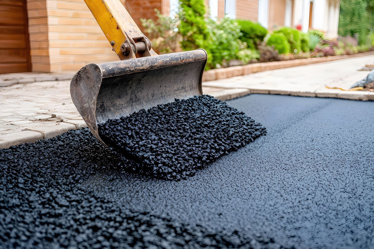 Excavator bucket spreading fresh black asphalt on a driveway. Excavator bucket spreading fresh black asphalt on a driveway.