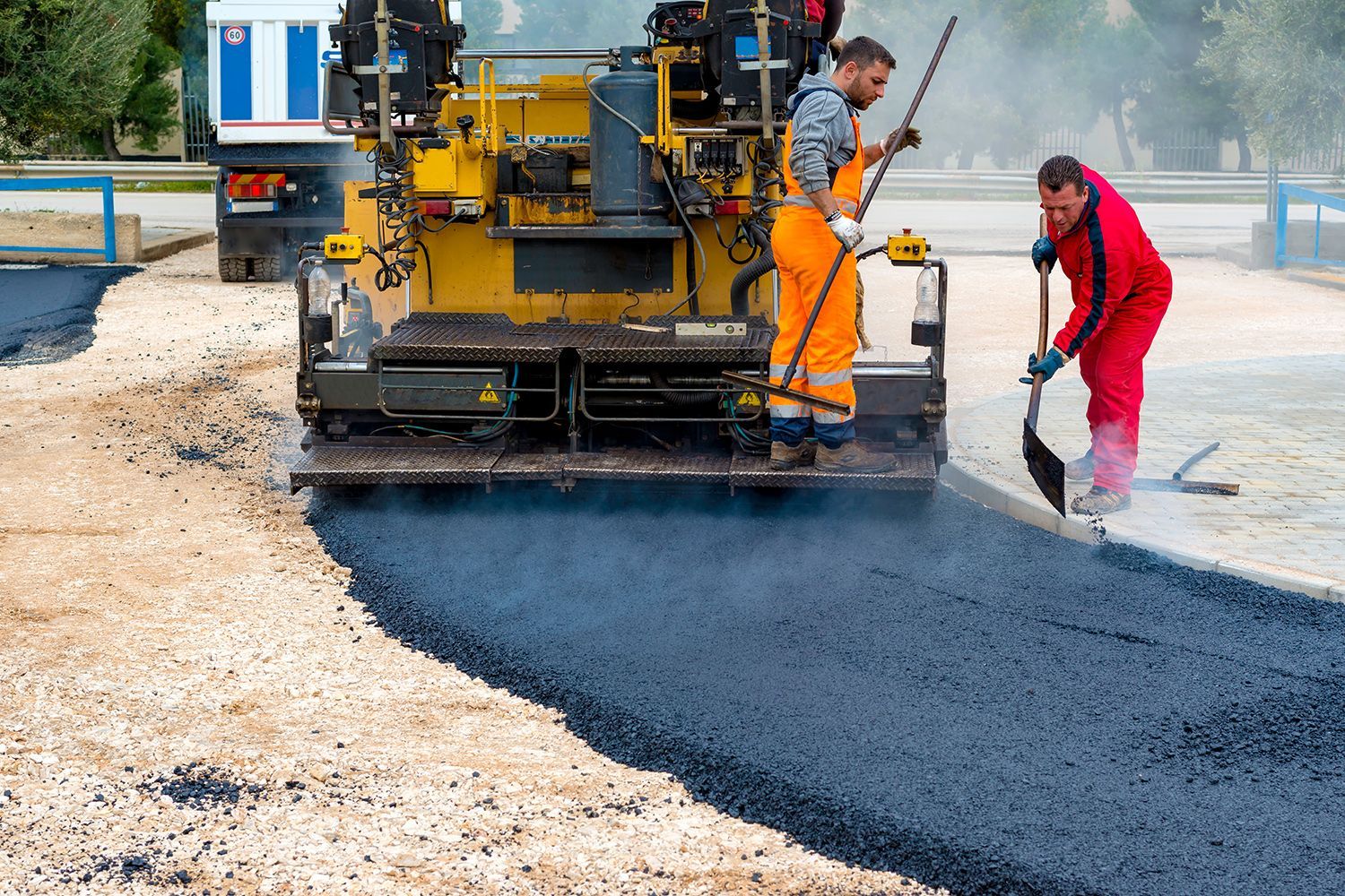 Asphalt paving machine laying blacktop with two workers nearby. Asphalt paving machine laying blacktop with two workers nearby.