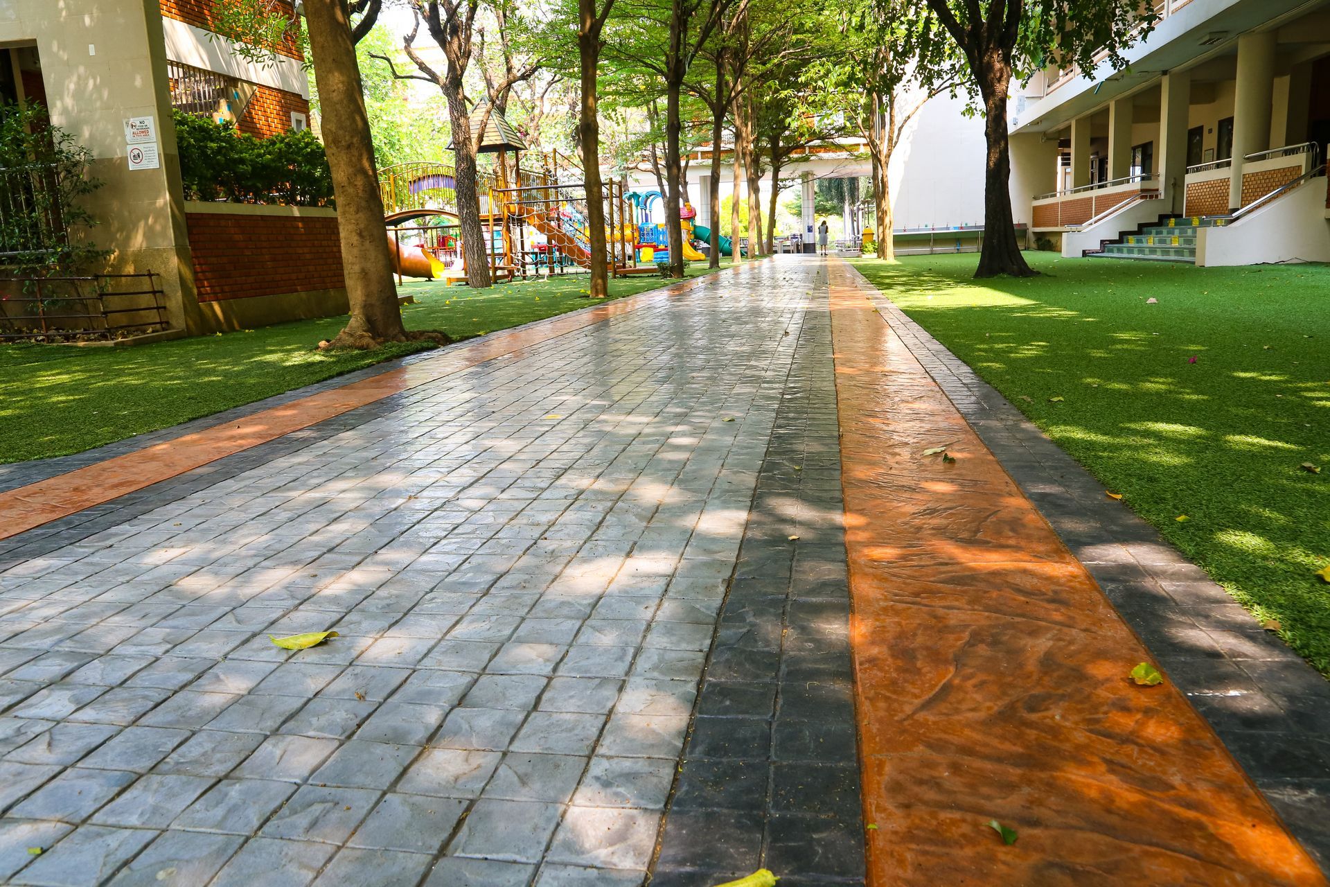 Brick pathway lined with orange and gray borders, trees, and green grass on both sides. Brick pathway lined with orange and gray borders, trees, and green grass on both sides.