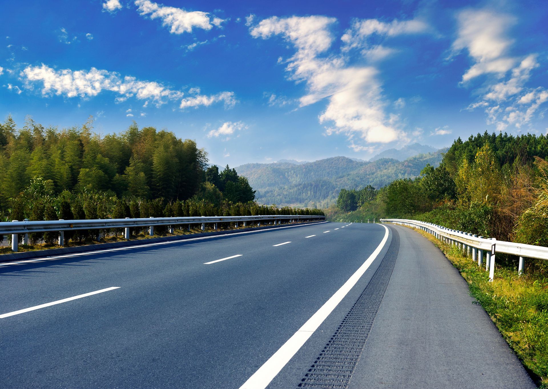 Road winding through a lush green landscape under a blue sky with fluffy clouds. Road winding through a lush green landscape under a blue sky with fluffy clouds.
