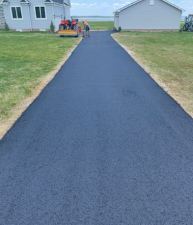 Person in orange workwear uses a long-handled asphalt rake on a newly paved road. Person in orange workwear uses a long-handled asphalt rake on a newly paved road.