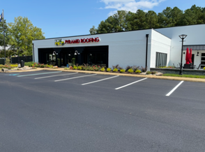 Empty asphalt parking lot with white painted lines; low grass border, modern building in background. Empty asphalt parking lot with white painted lines; low grass border, modern building in background.