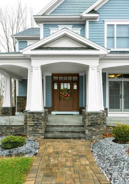 Front porch of a blue house with stone steps, white columns, and a wooden door with a wreath.