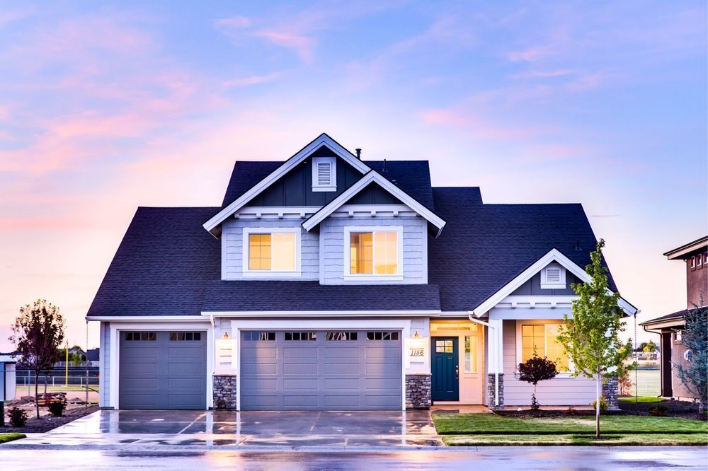Modern two-story suburban house with lit windows and a wet driveway at sunset