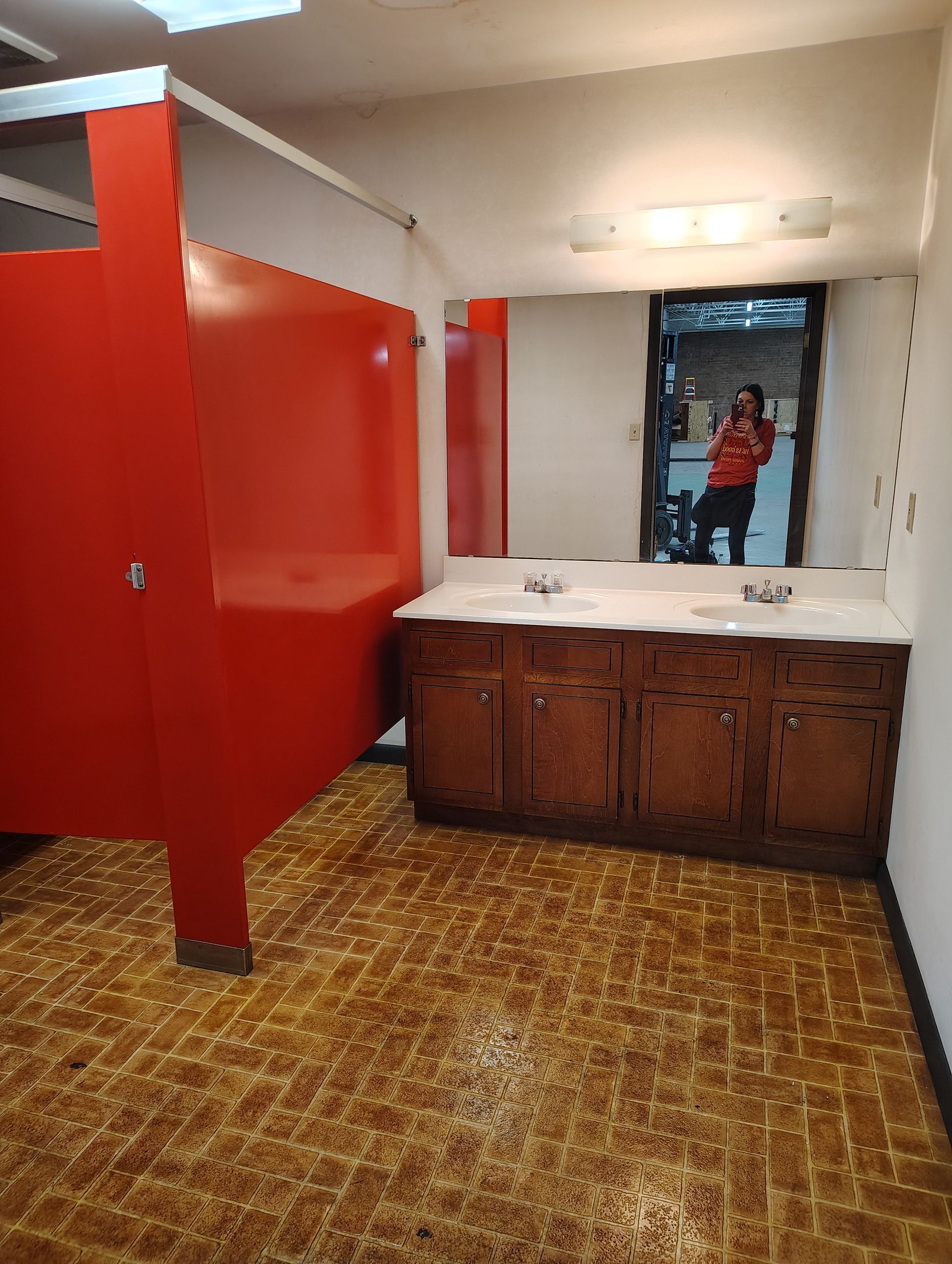 Red restroom with stalls, sinks, and a person reflected in the mirror.