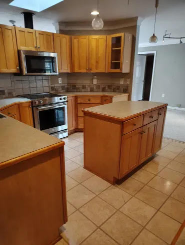 Empty kitchen with wooden cabinets, tiled floor, and a central island under pendant lights.