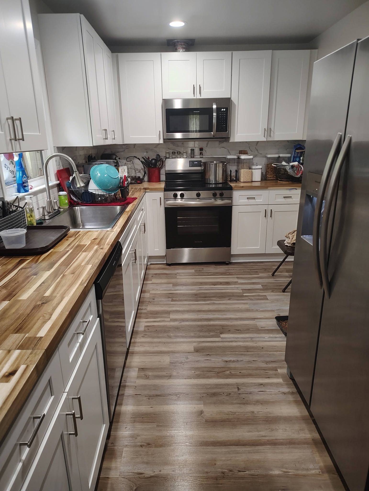 Modern kitchen with white cabinets, stainless steel appliances, and a wood-look floor.