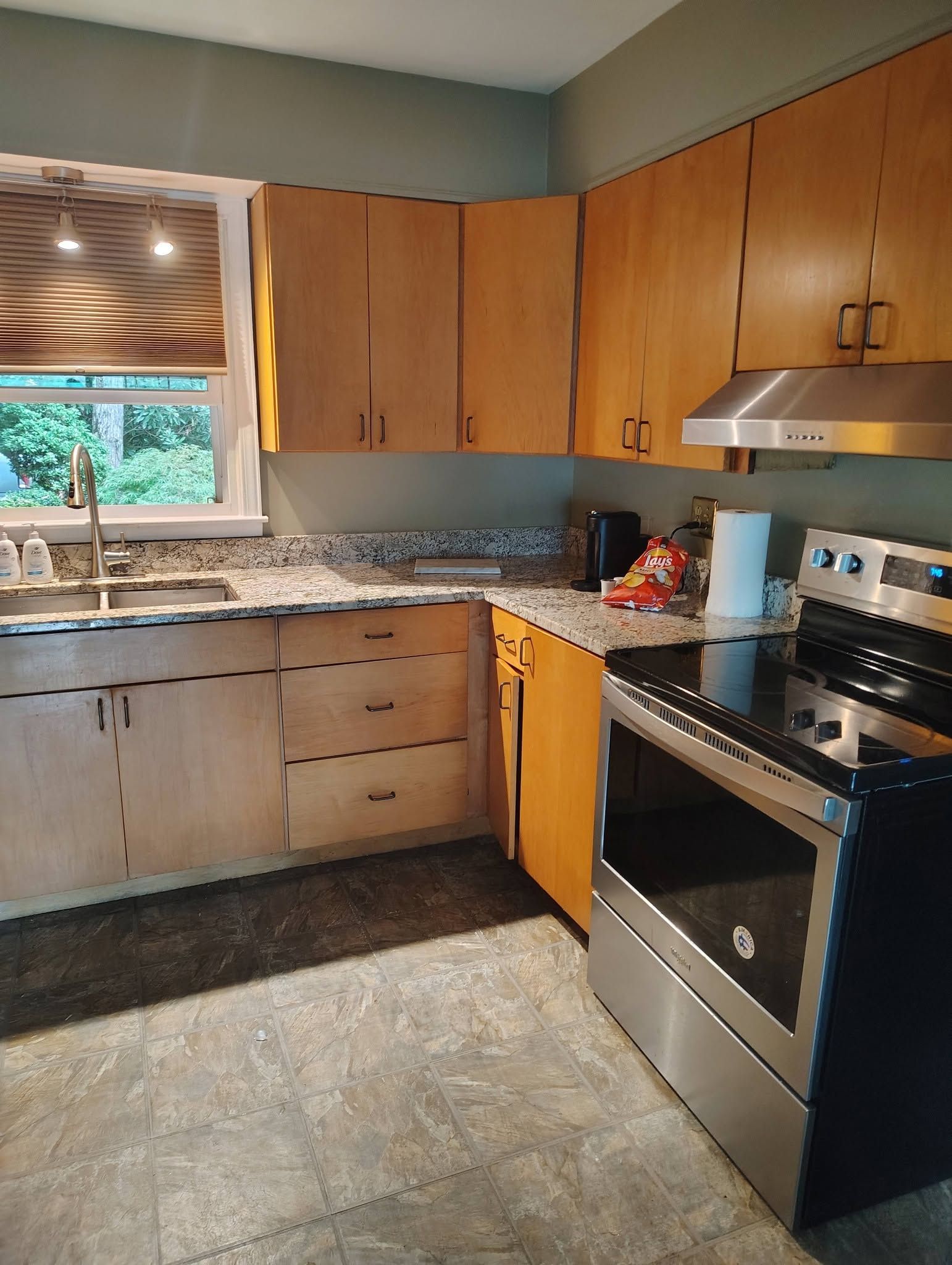 Modern kitchen with wood cabinets, black appliances, gray tile floor, and a window over the sink