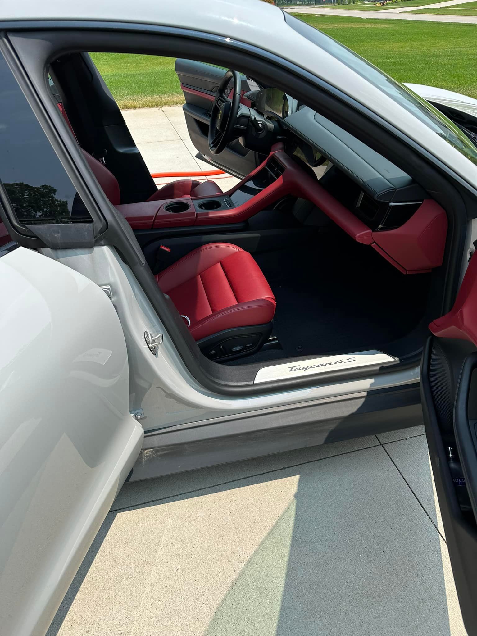 Gray Porsche Panamera with red interior, door open, parked on a paved driveway.