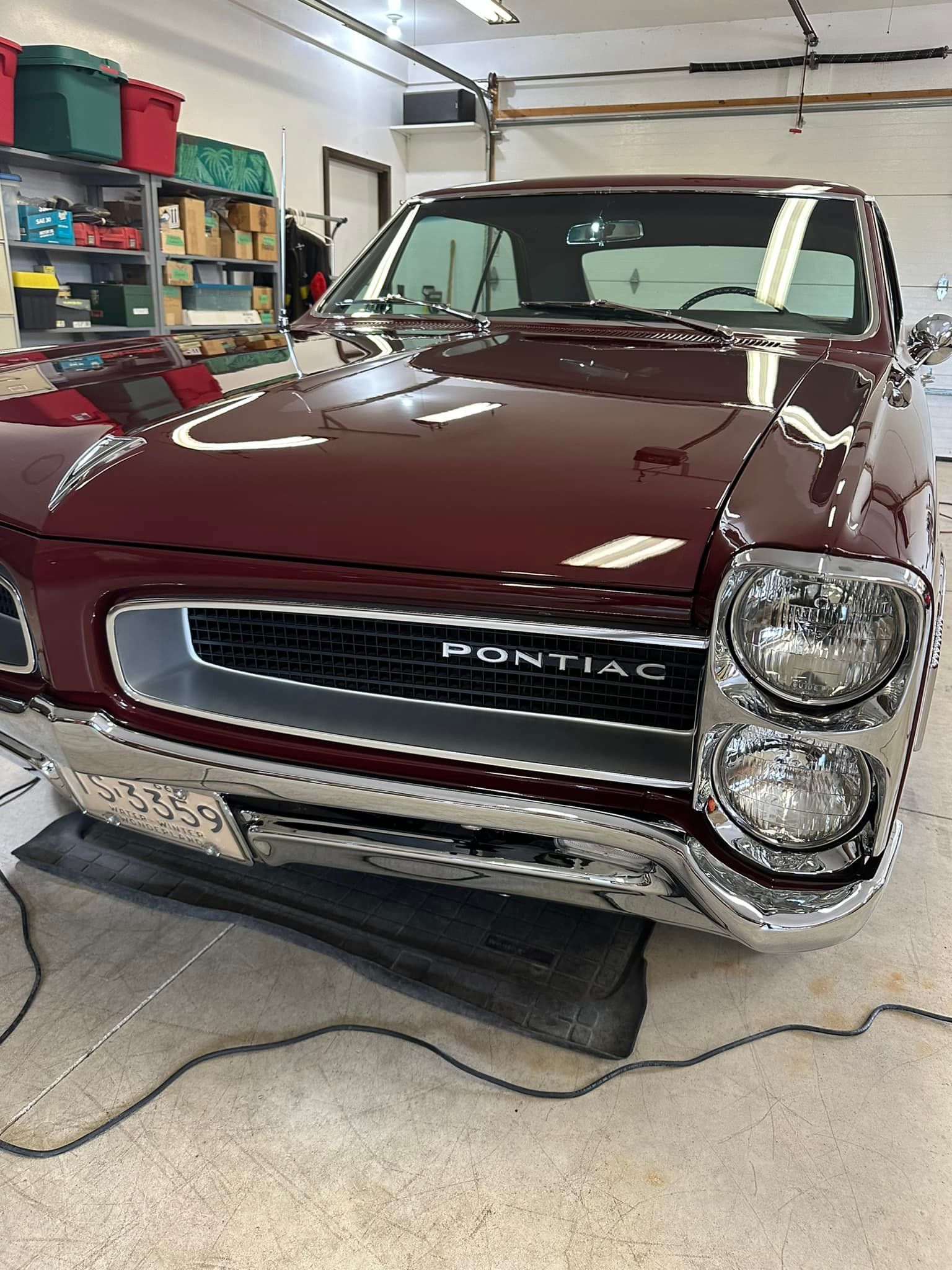 Burgundy 1965 Pontiac GTO in a garage, shiny chrome grill and headlights.