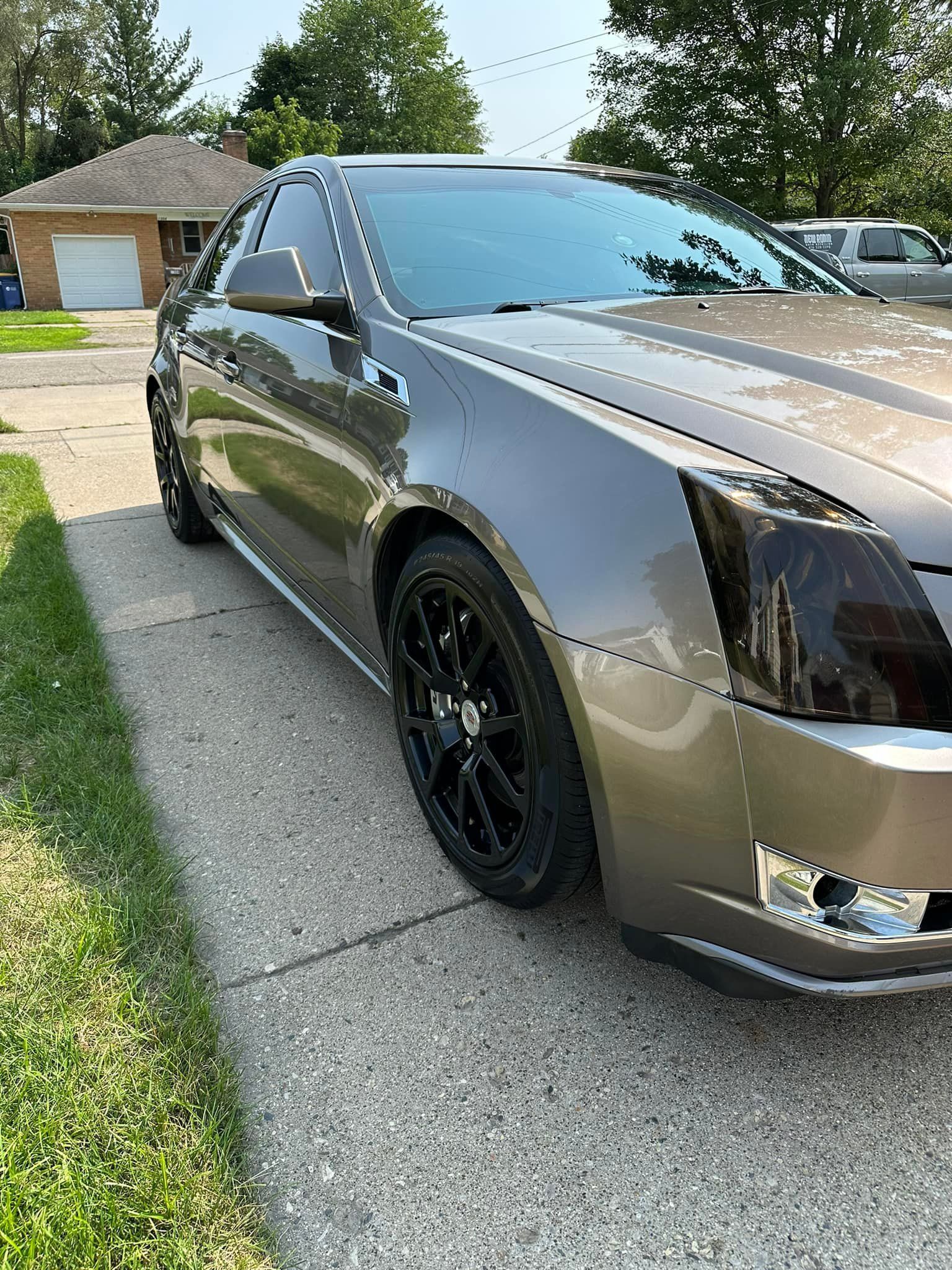 A bronze Cadillac CTS coupe parked on a driveway with black rims and tinted headlights.