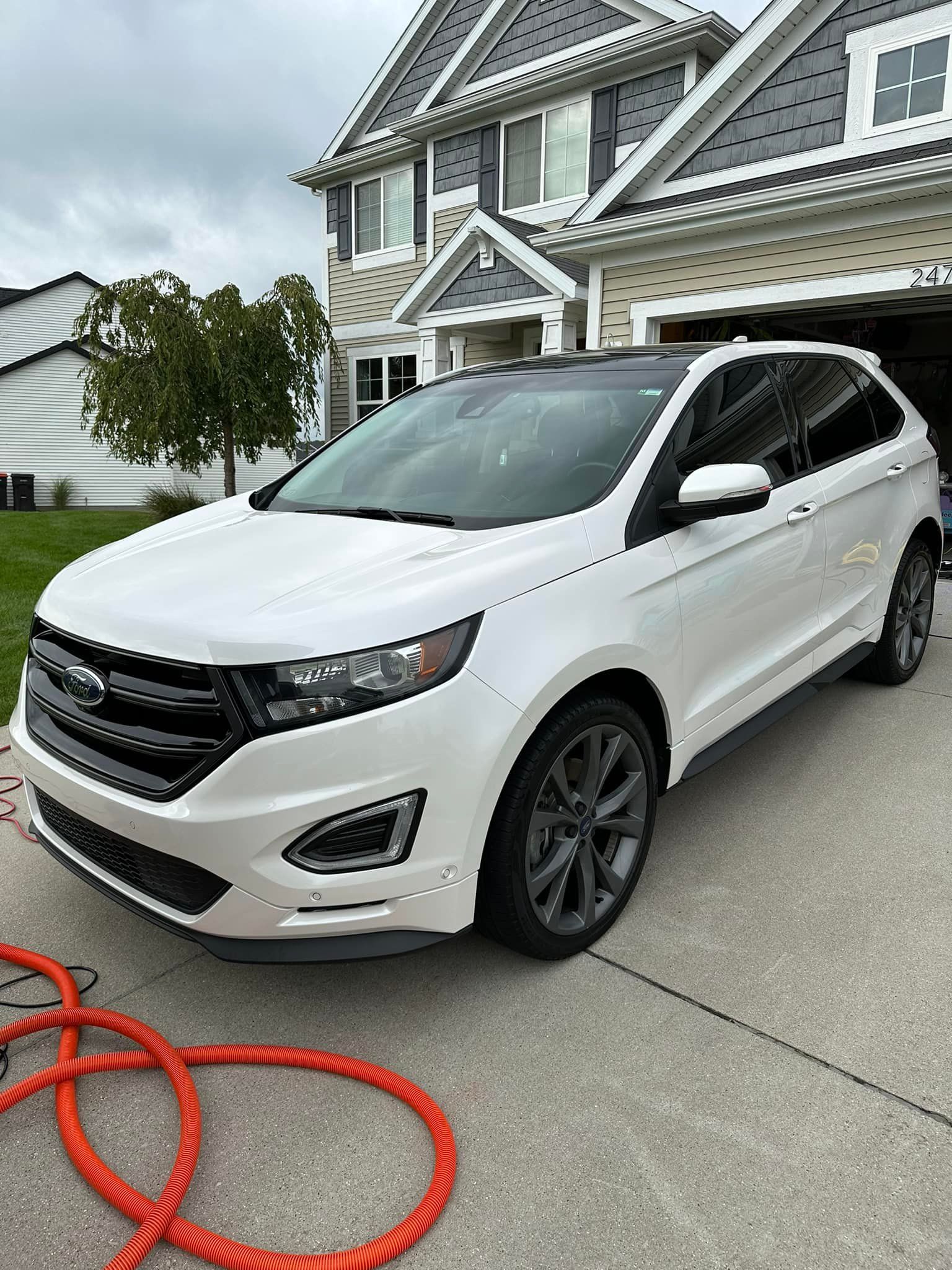 White Ford Edge SUV parked in a driveway in front of a house. Black roof and gray wheels.