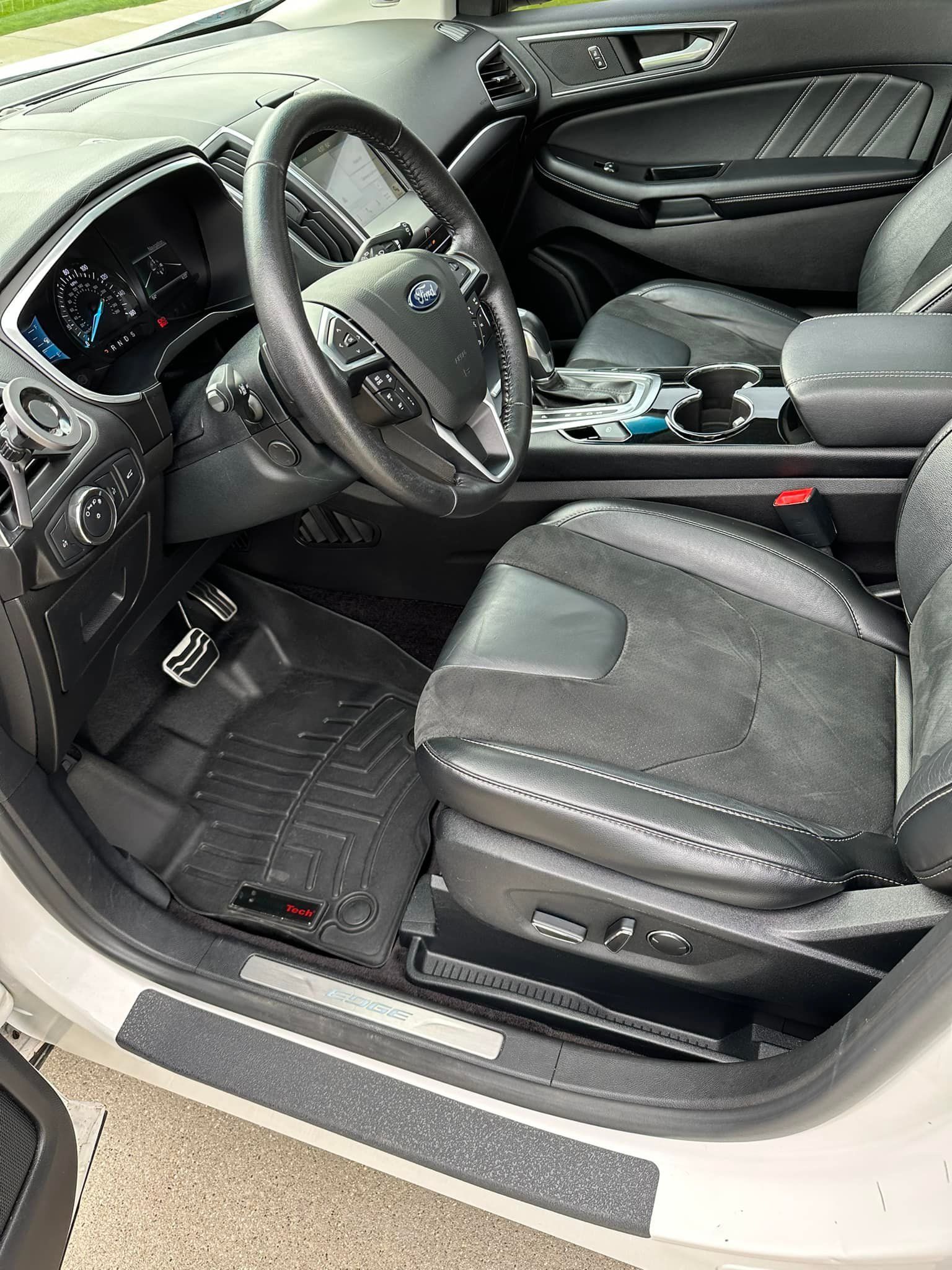 Interior view of a Ford Edge, showing the driver's seat, steering wheel, dashboard, and floor mats.