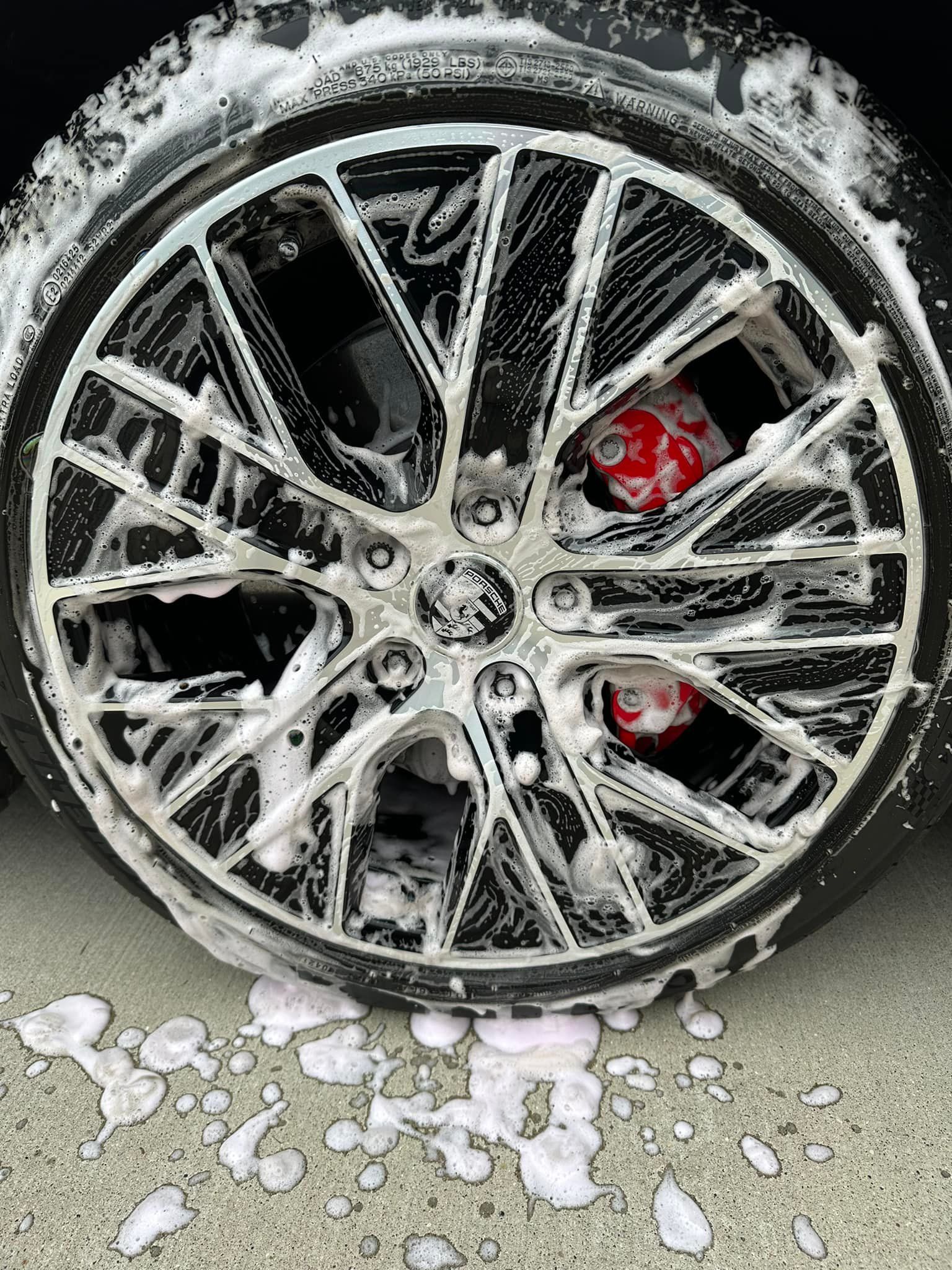 Car wheel covered in white soap suds; a red brake caliper is visible.