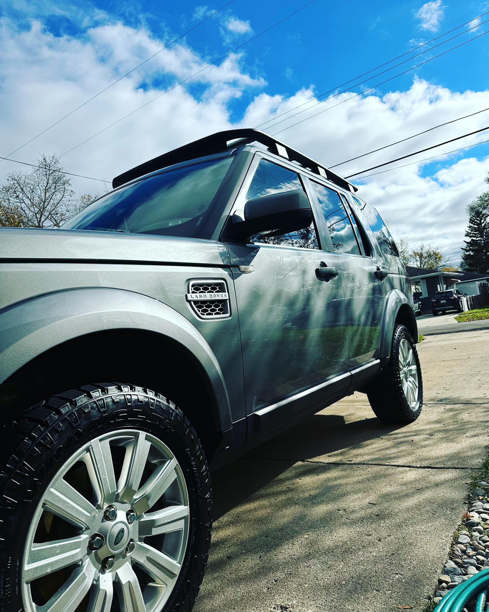 Silver Land Rover SUV parked on a paved road under a partly cloudy sky.