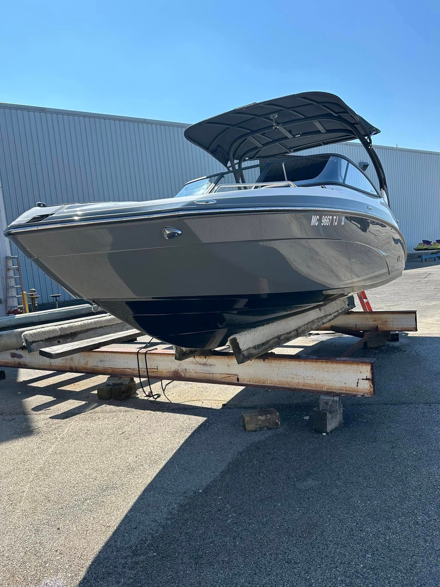 Gray motorboat on a trailer, under a black canopy. Outdoors on pavement.