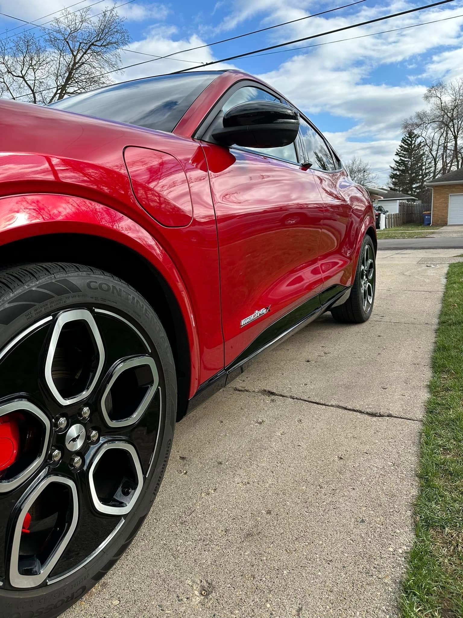Red Ford Mustang Mach-E parked on a driveway, black wheels, against a blue sky.