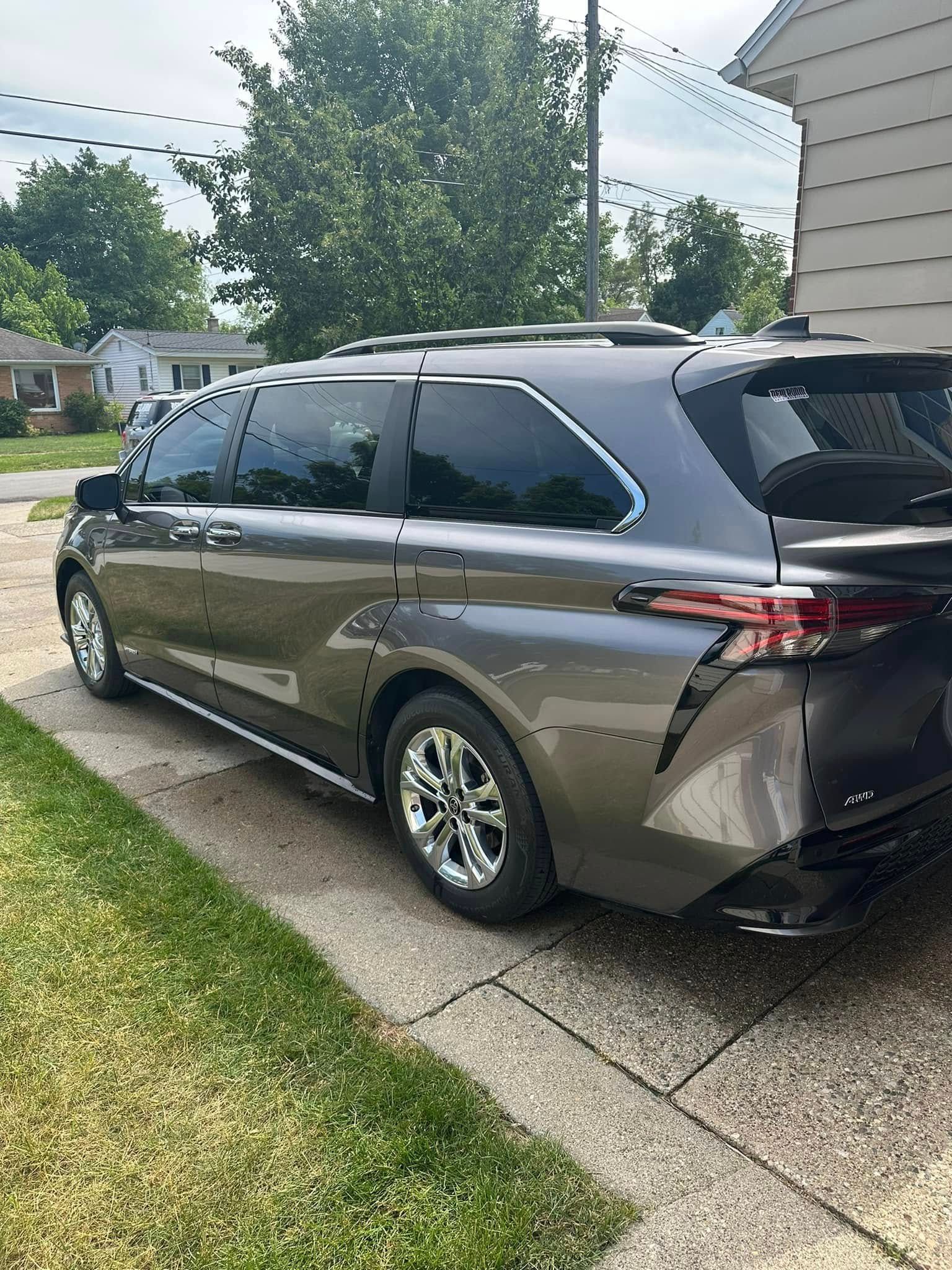 Gray minivan parked on a driveway next to a grassy lawn, near a house.