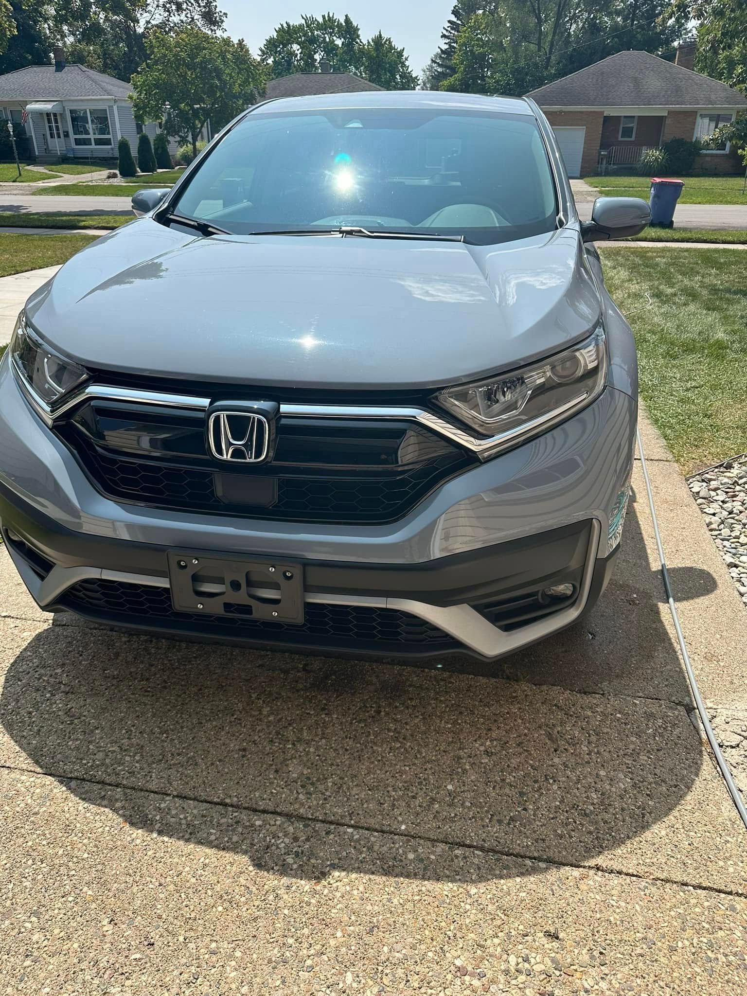 Gray Honda CRV parked on a concrete driveway in front of a house on a sunny day.