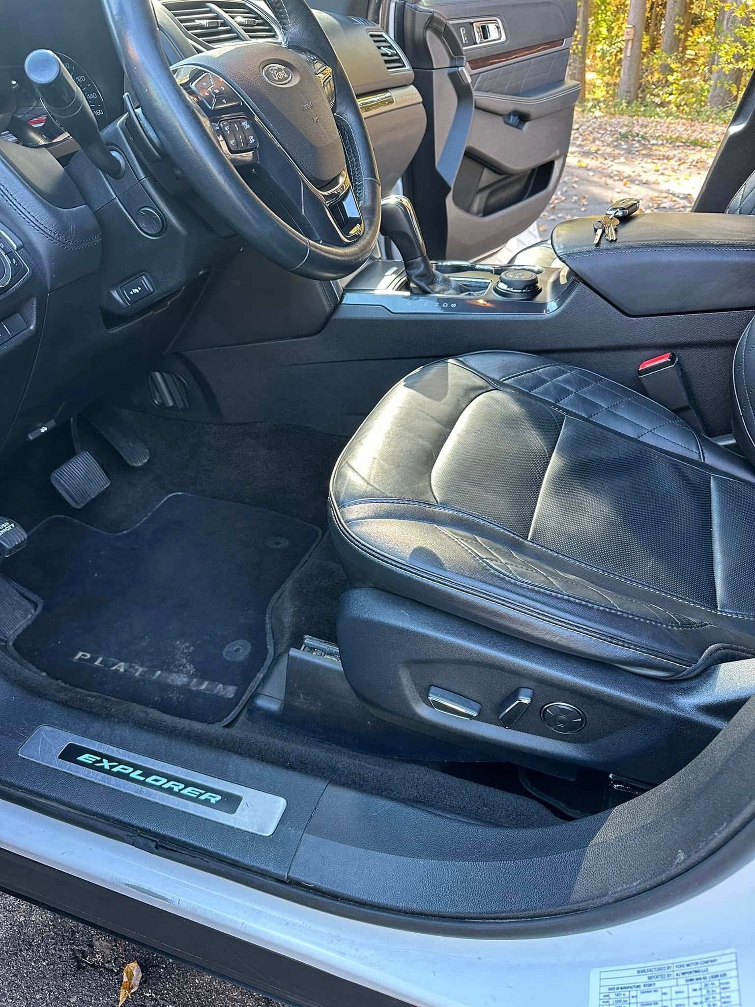 Interior of a black leather car with a black steering wheel, seat and floor mats. A door is open.
