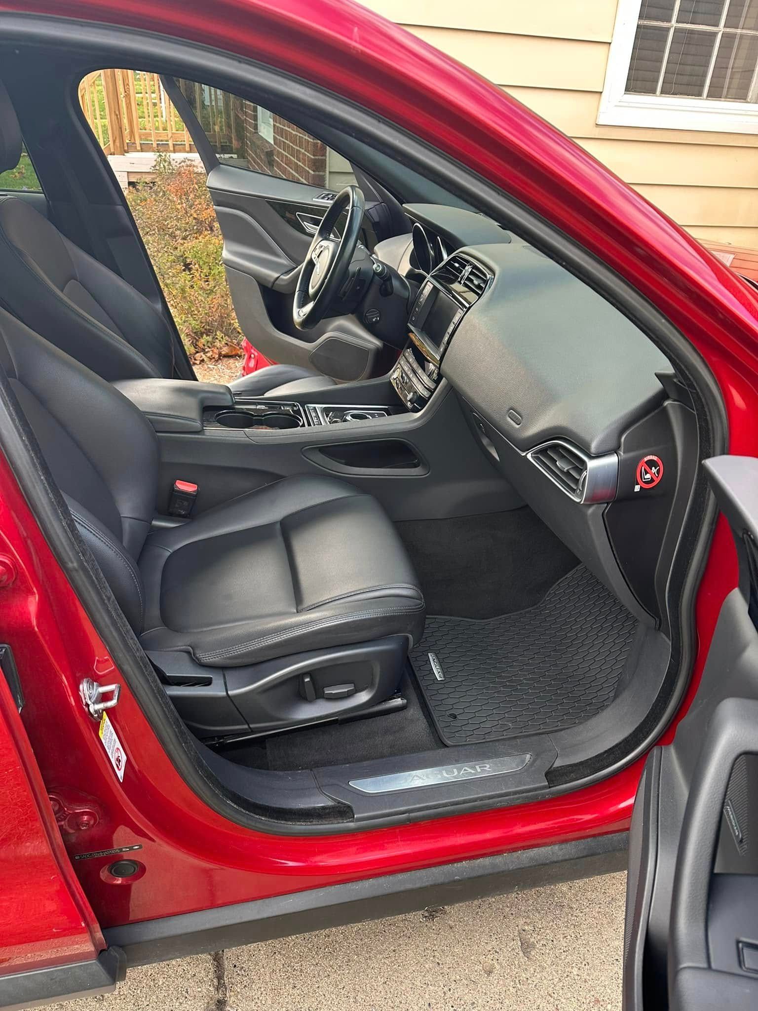 Red Jaguar car interior with black leather seats and dashboard, open door.