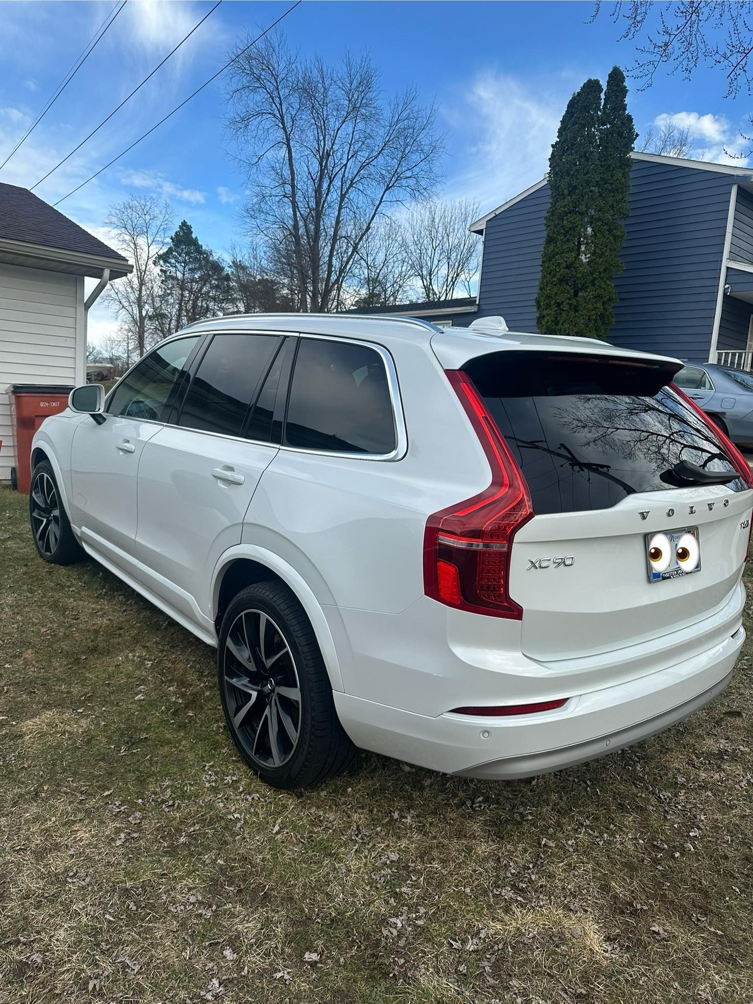 White Volvo XC90 SUV parked on grass, with tinted windows, black wheels, and a blue sky in the background.