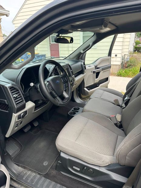 Interior of a black Ford pickup truck, driver's side door open, seats are grey patterned.