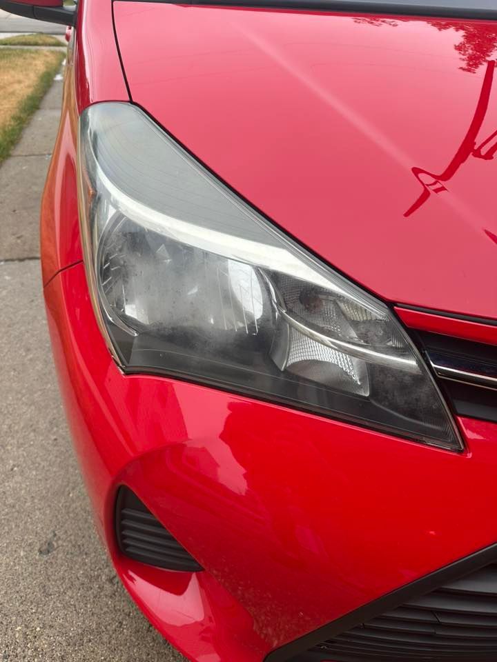 Red Toyota Yaris car front; close-up of headlight and hood; parked outdoors.