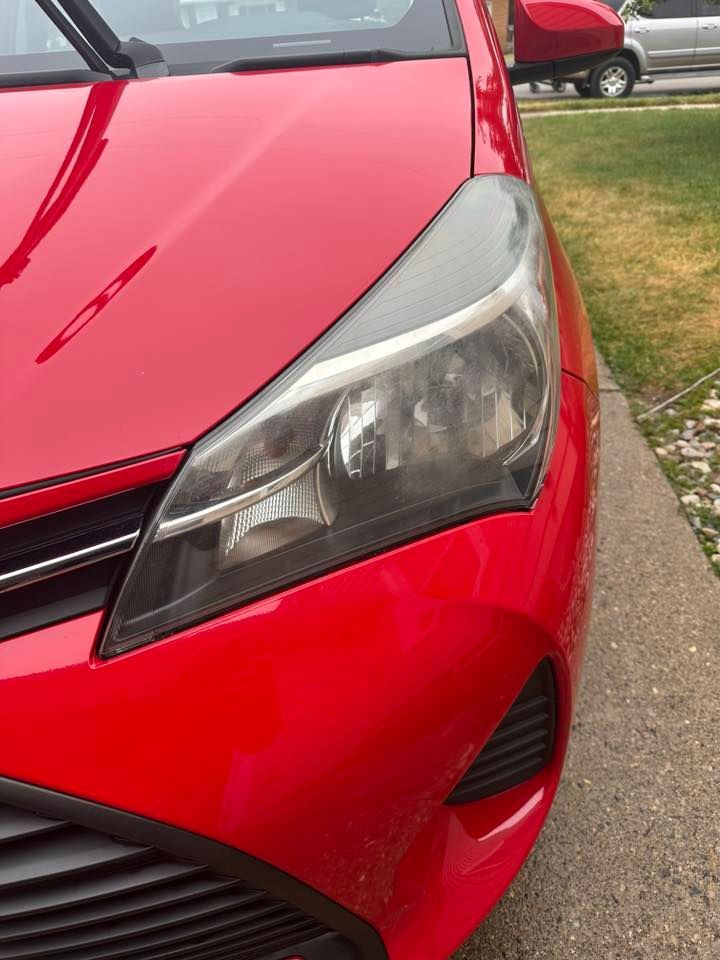 Red Toyota Yaris car front, right headlight is cloudy.