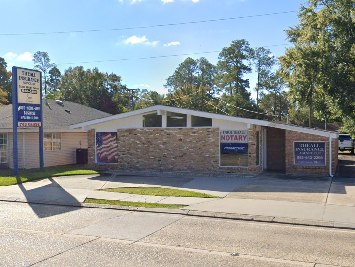 Small brick storefront with American flag mural, notary sign, and parking lot in front