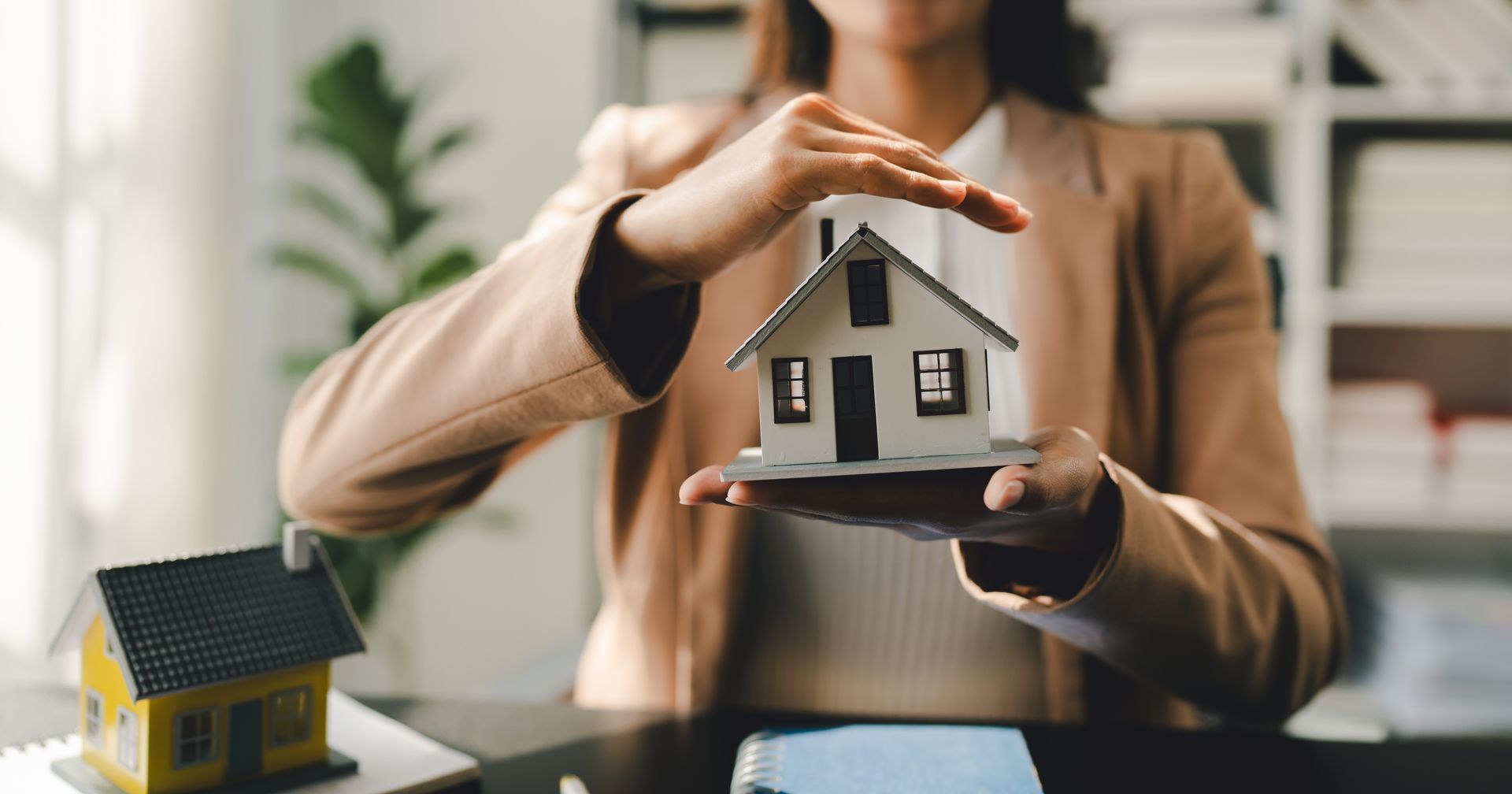 Person holding a small house model above a desk with another house model in the foreground