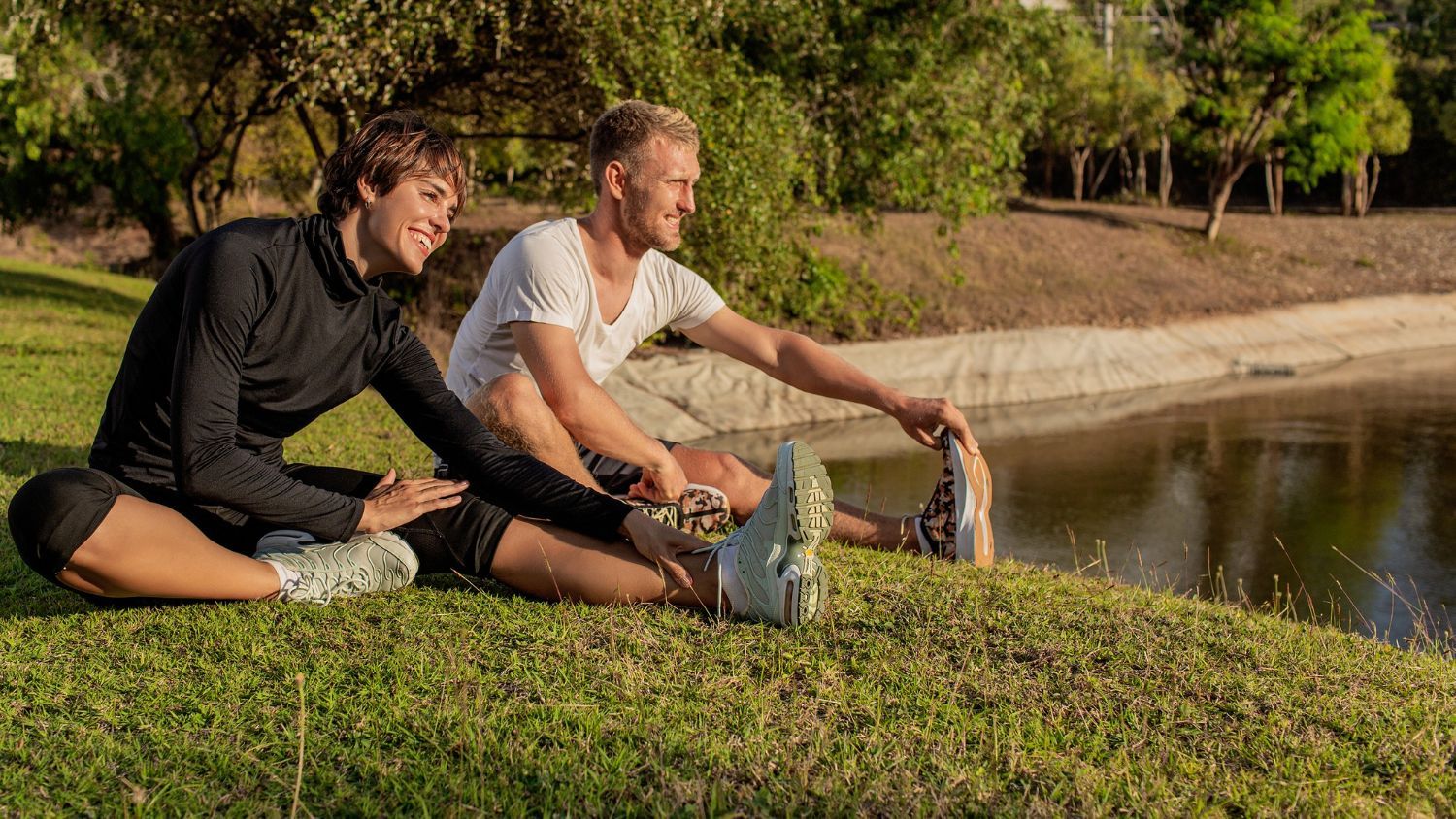 A man and a woman are sitting on the grass stretching their legs.