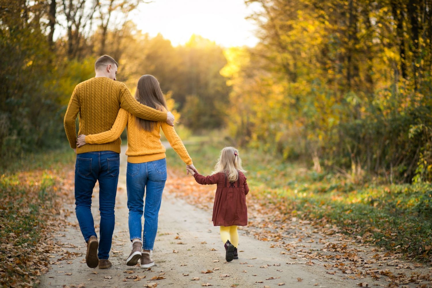 A family is walking down a path in the woods holding hands.