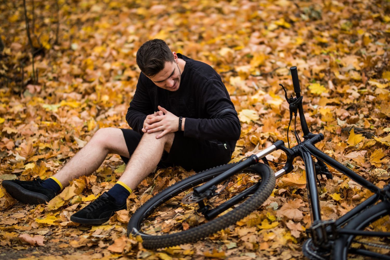 A man is sitting on the ground with his knee in pain next to a bicycle.
