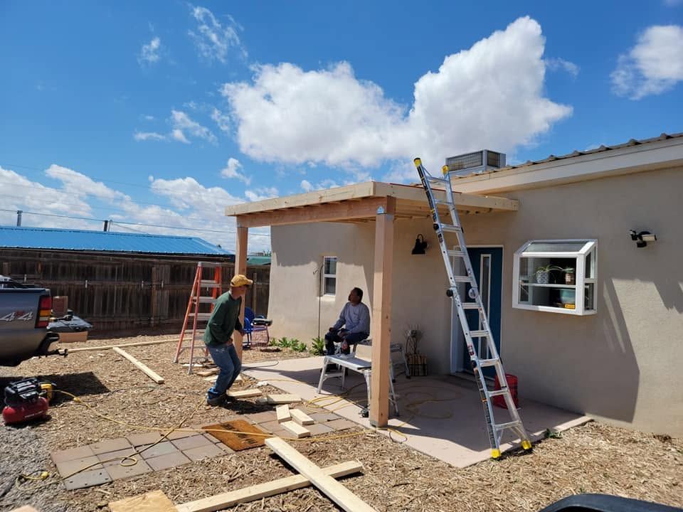Workers repairing a house roof and patio under a blue sky, with a ladder and construction materials nearby