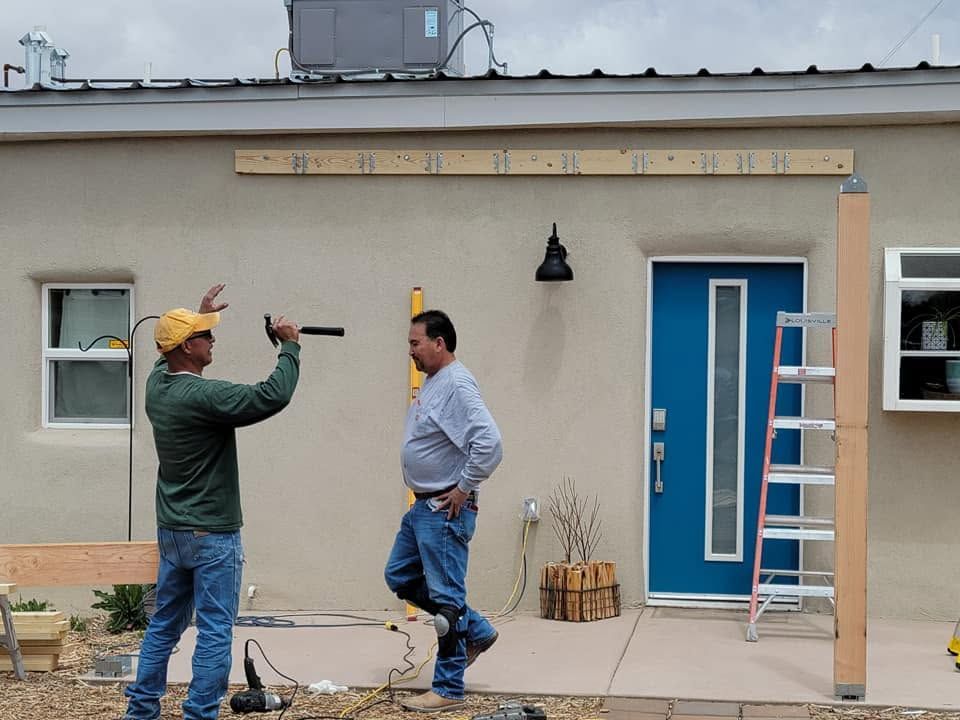 Two workers measuring a house exterior near a blue door and a ladder