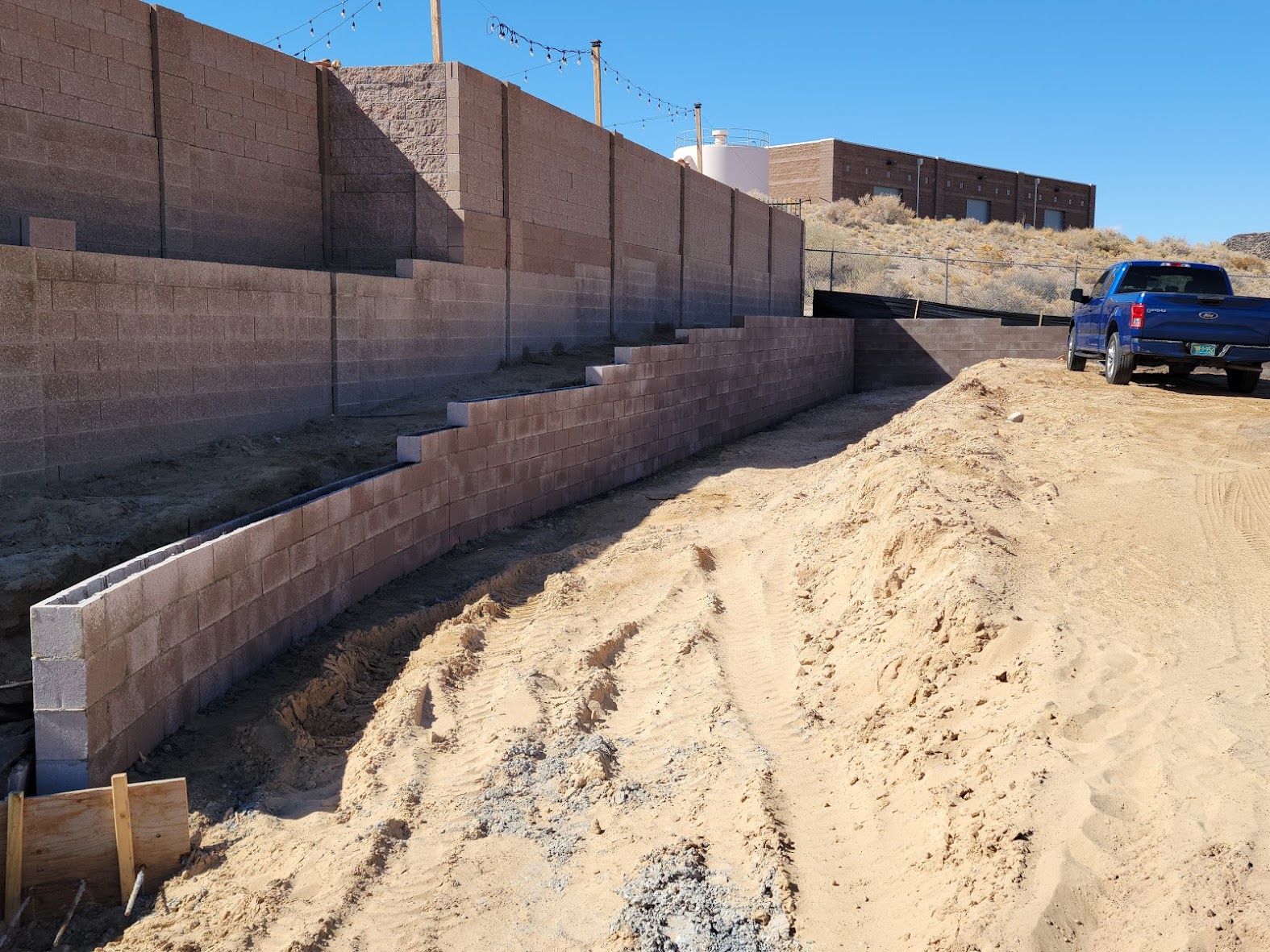 Roadside retaining wall under construction with concrete blocks, traffic cones, and construction materials