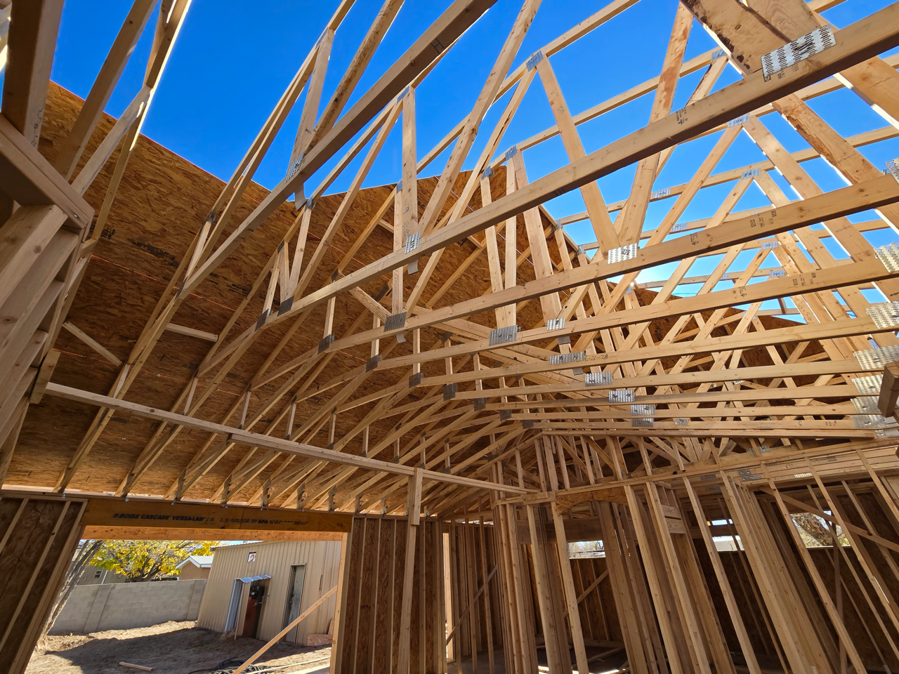 Partially built house with exposed wooden roof framing and OSB siding at a construction site.