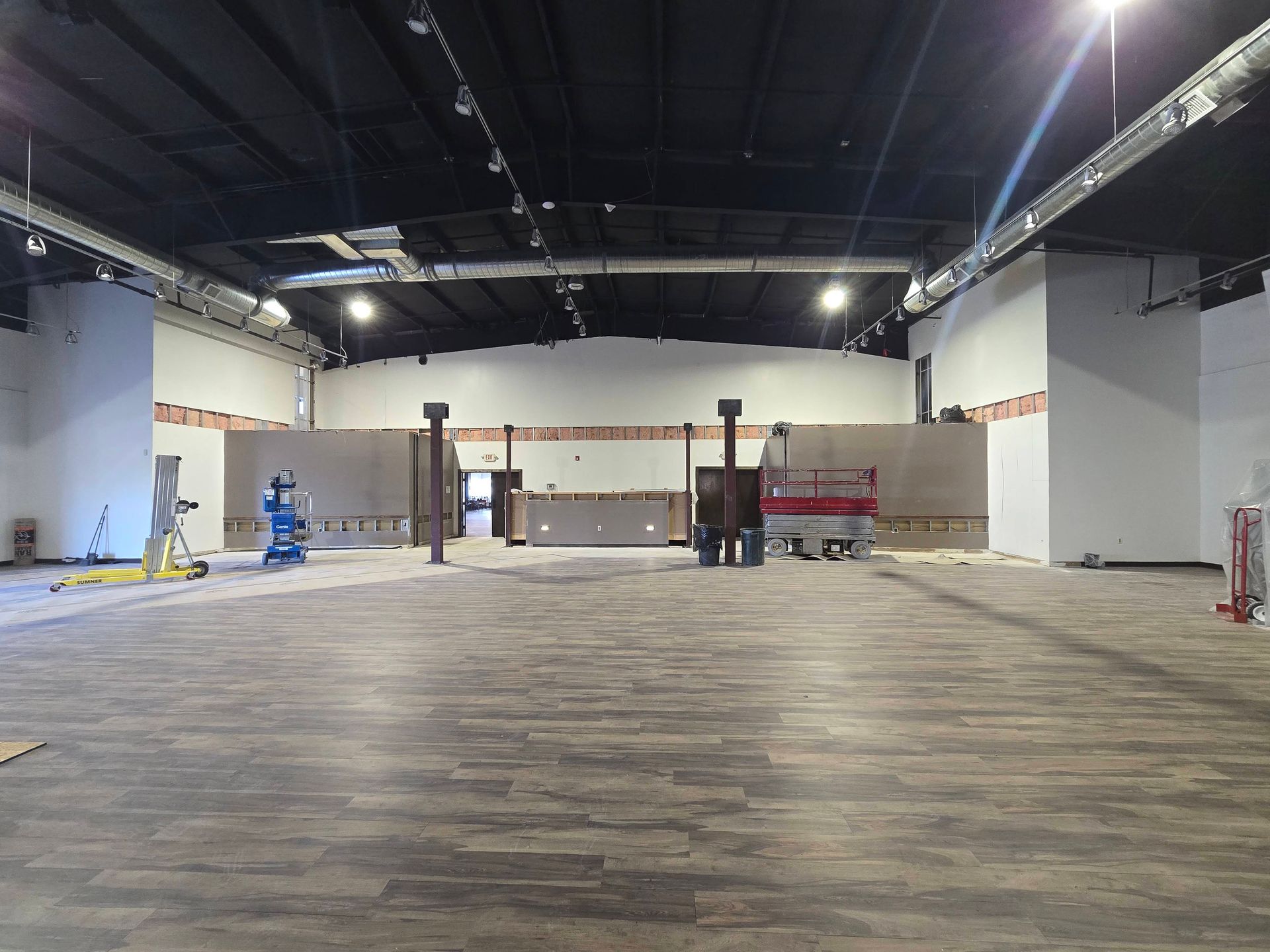 Empty commercial space with carpeted floor, exposed ceiling, and a few work benches and carts לאורך the back wall