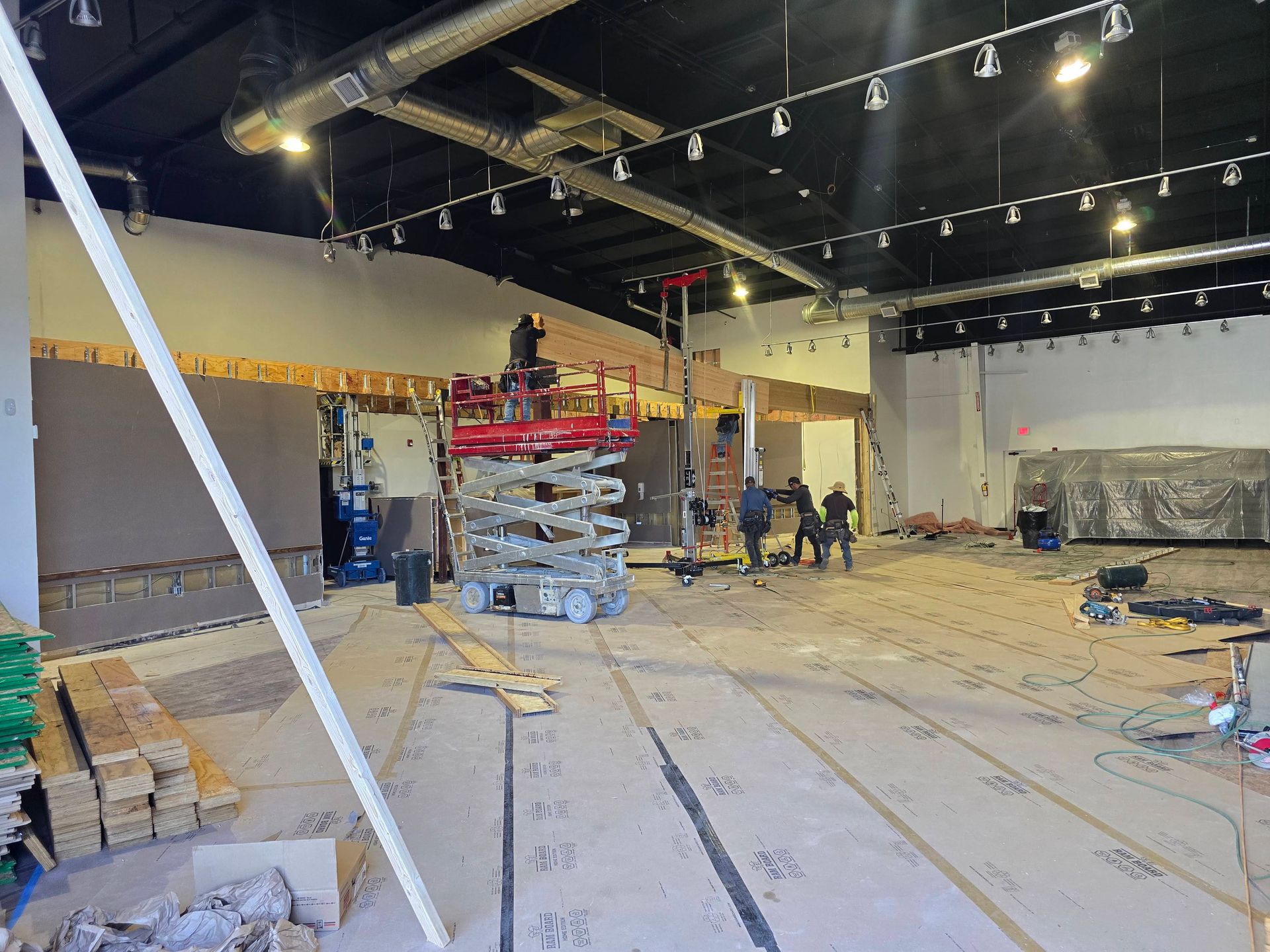 Large vacant warehouse interior with exposed ceiling lights, scaffolding, and people working in the distance.