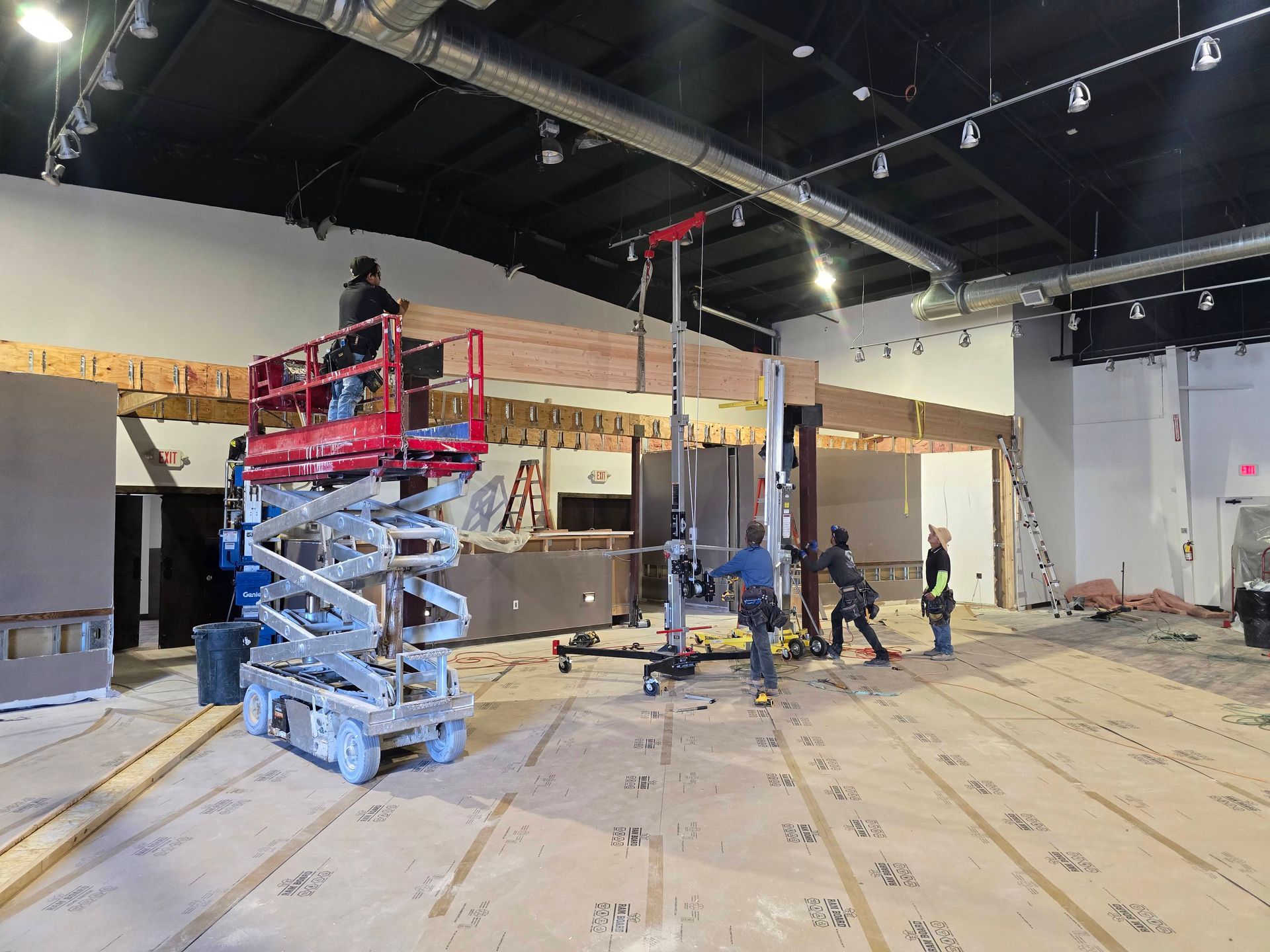 Workers using scissor lifts inside a large unfinished room with exposed ceiling and materials on the floor